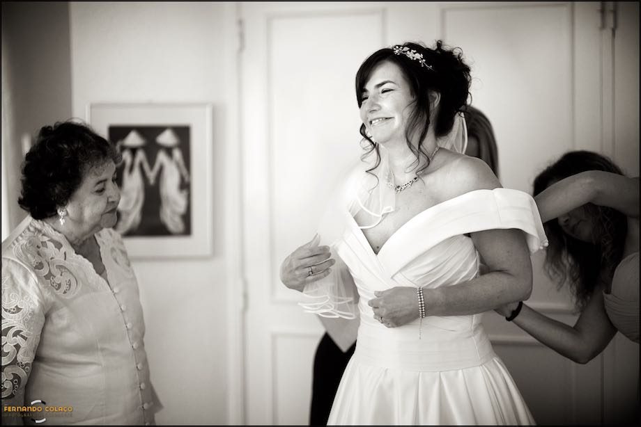 The bride's mother looks at her as two friends button her dress.