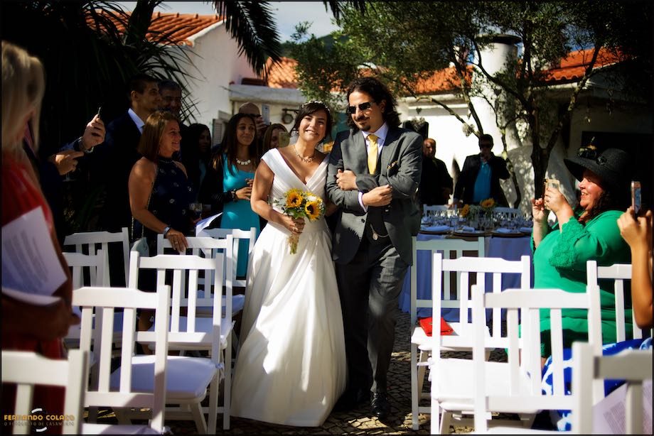 The bride enters the place of the wedding ceremony, among the guests, arm in arm with her eldest son.