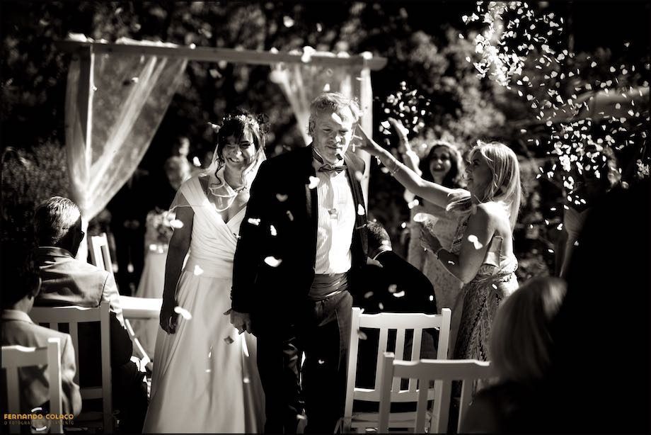 The bride and groom, holding hands, leave the ceremony under flower petals at Morada do Sol in Malveira, captured by the wedding photographer in Sintra.