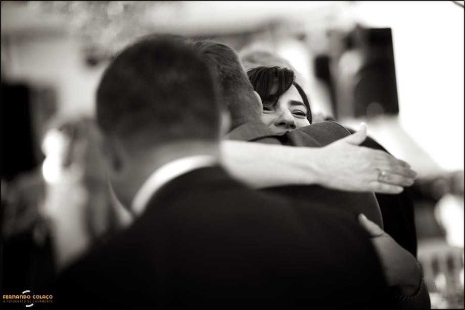 The bride's face appears over the shoulders of a wedding guest who hugs her as he congratulates her on the wedding.