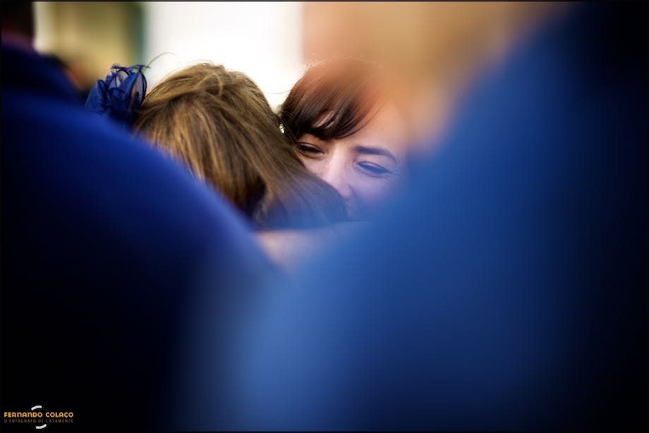 Amid blurred wedding guests, the bride's face as she hugs a guest.