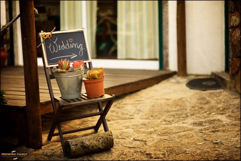 Slate sign indicating the location of the wedding, on a chair with two potted cacti.