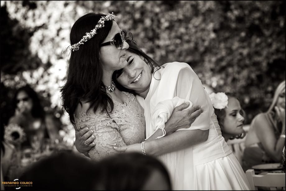 The emotional bride leans her head on the shoulders of a female friend at the wedding reception.