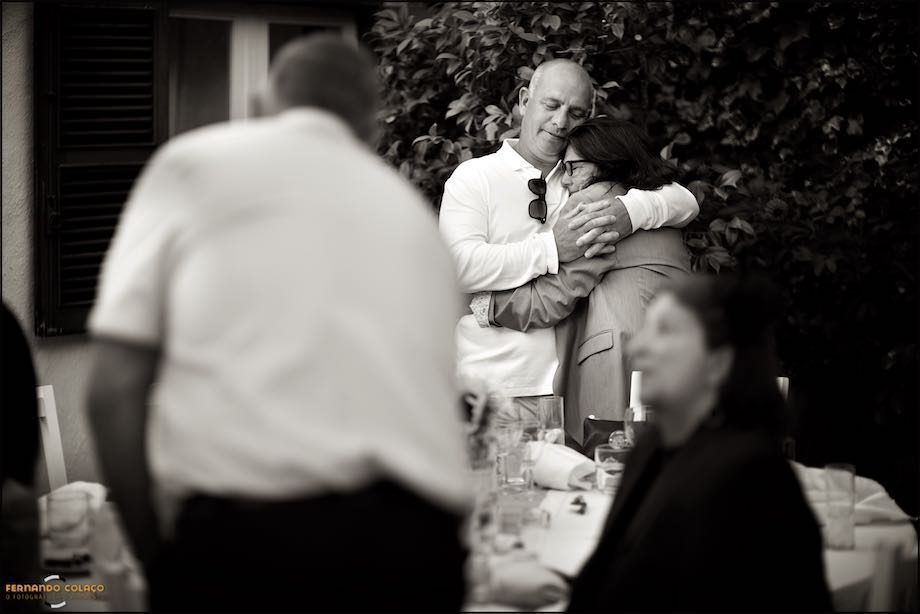 A couple of guests at the wedding, next to an orange tree in the garden of Morada do Sol in Sintra and among other friends, embrace each other with emotion.