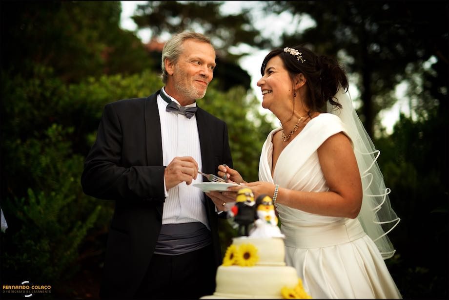 The bride and groom, looking at each other and laughing, taste the wedding cake.