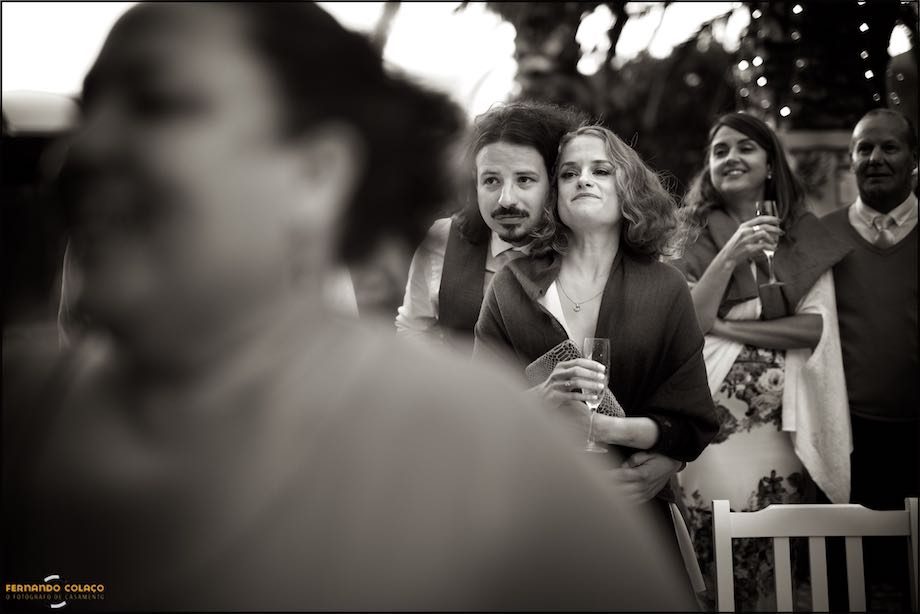 A couple of wedding guests, embraced and among other guests, watch the cutting of the cake by the bride and groom at Morada do Sol in Sintra.