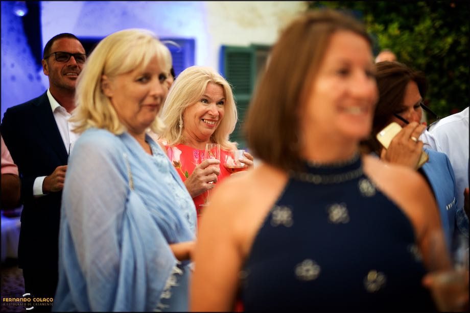 A female wedding guest, among others, out of focus, smiles while watching the wedding cake being cut.