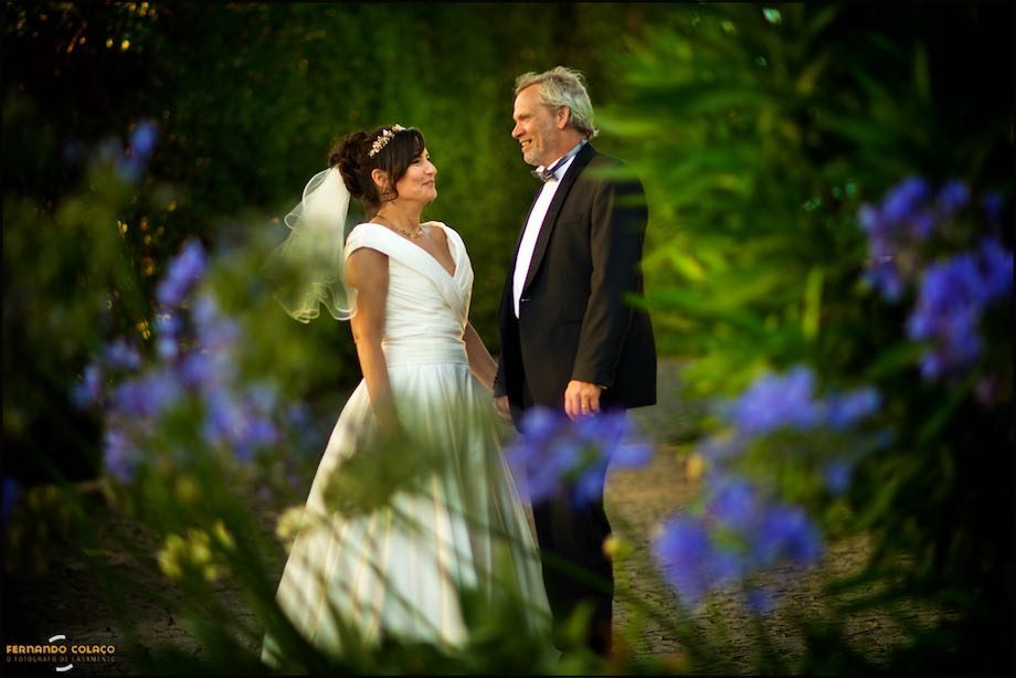 In the garden of Morada do Sol in Sintra, the bride and groom, facing each other, smiling, with blue flowers in the foreground, out of focus.