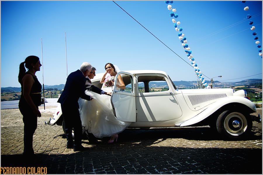 A noiva sai da automóvel antigo, no largo da igreja para entrar para a cerimónia do casamento.