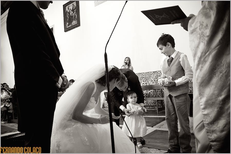 Uma menina quase bebé, junto do seu irmão, já um rapaz, entregam aos noivos as alianças do casamento, juntos dos noivos e do padre.