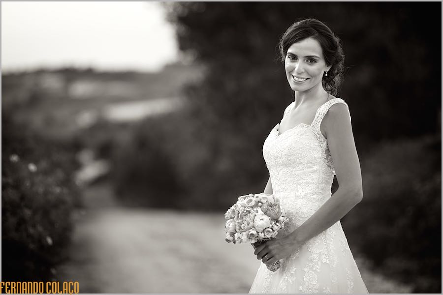 A noiva sorrindo e com o bouquet na mão, num caminho junto da Casa de Reguengos, num retrato pelo fotógrafo de casamento.