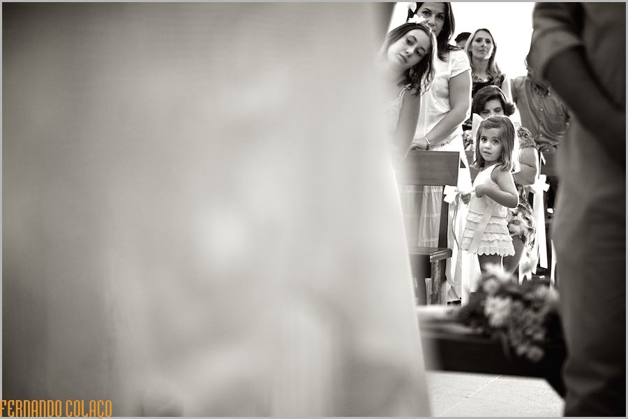 Girl, among guests at the wedding ceremony, looks ahead as seen through the newlyweds, out of focus.