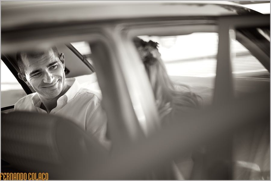 Inside the car, the groom smiles happily at the bride before leaving for the wedding reception venue.