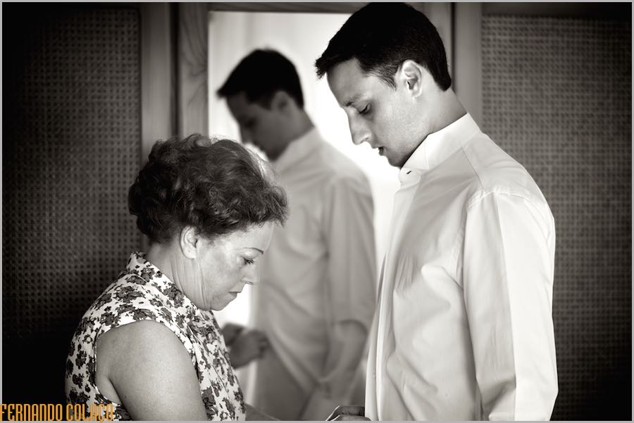 The groom with his mother who helps him to button his shirt, when dressing for the wedding.
