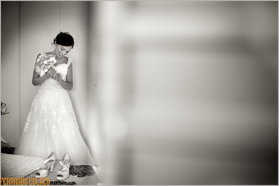 With her dress already on, the bride, with the bouquet in her hand, looks down.