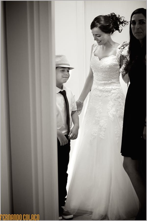 The bride, already prepared to leave for the wedding ceremony, talks to the little boy with the hat on his head.