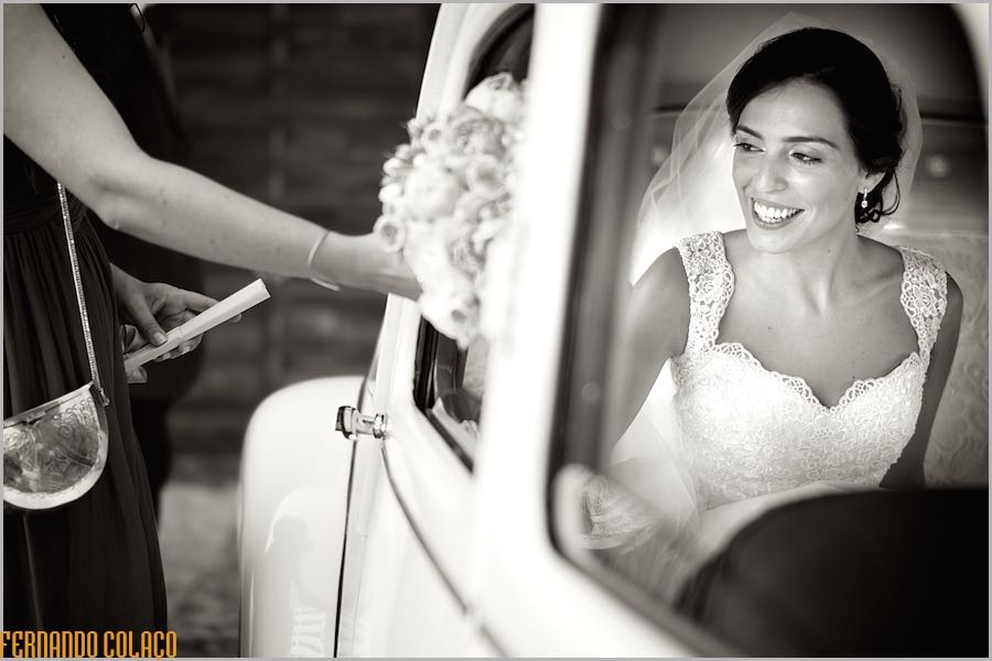With the bride, smiling, already inside the old car, a hand gives her the bunch of flowers.