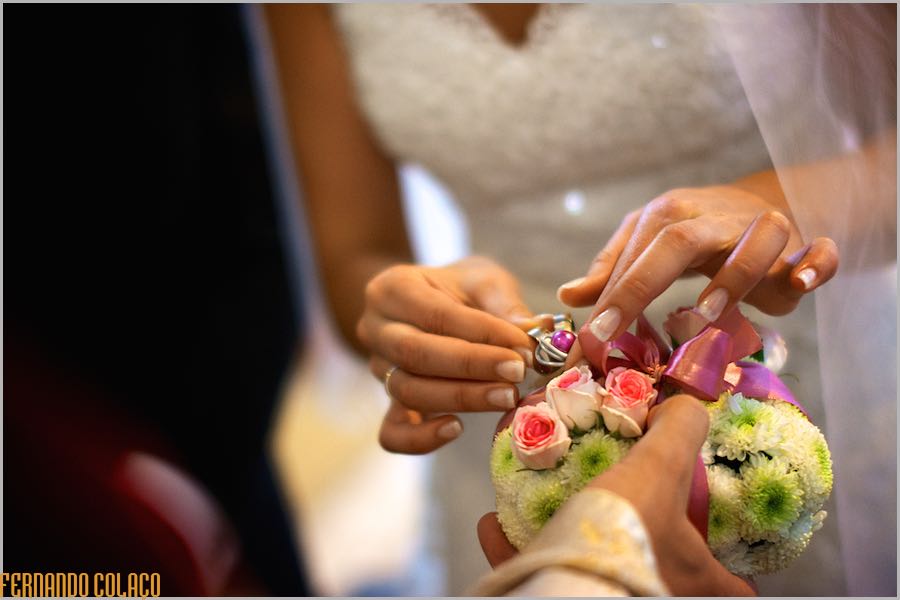 Groom's hand holds the floral arrangement with the rings while the bride's hand removes the rings.