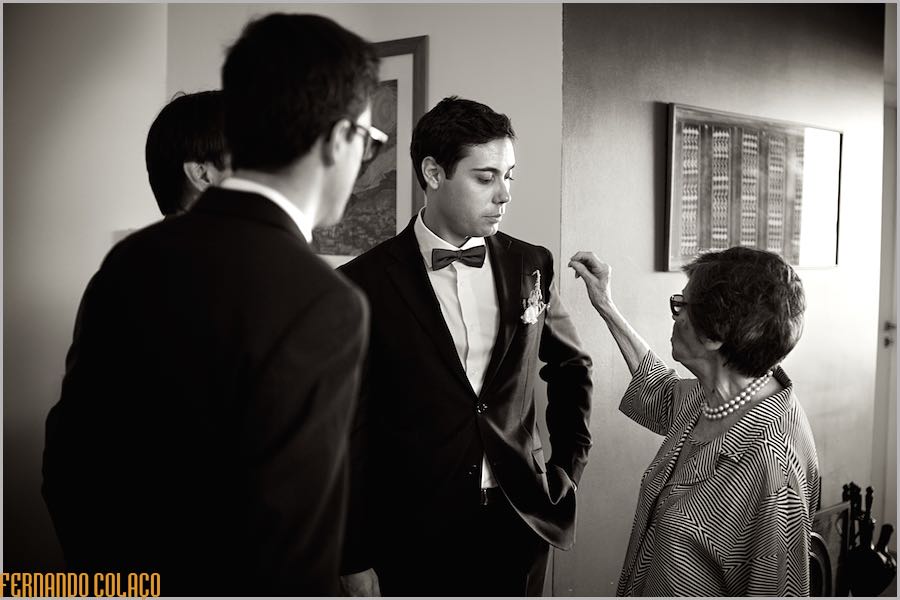The groom, after dressing for the wedding, with two friends and the grandmother who arranges the small bunch of flowers in the lapel of his coat.
