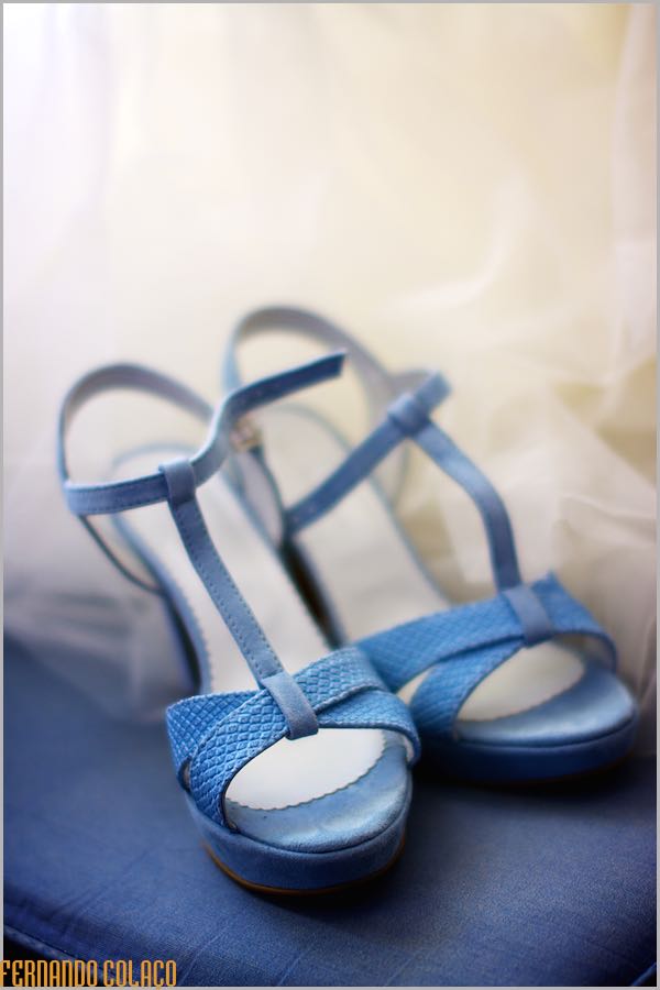 The bride's blue shoes, on the fabric of a sofa and with the bride's veil behind.