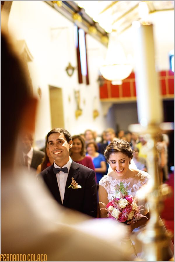 Already married, the bride and groom laugh at the priest, in front of them, out of focus.