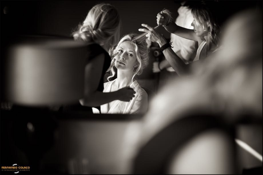 Noiva no meio da maquilhadora e da cabeleireira num espelho.