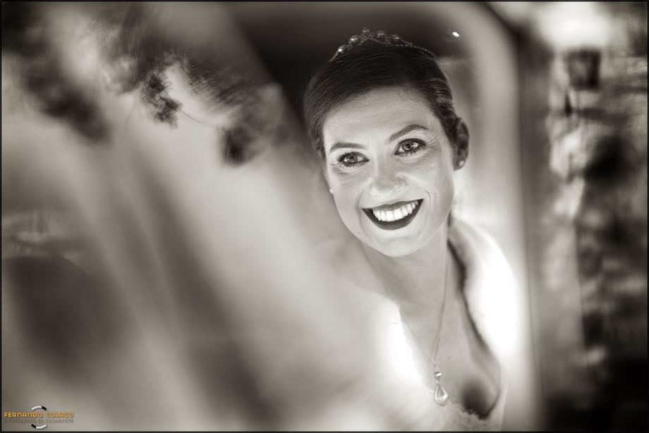 Bride smiles, inside the car, for the wedding photographer that he takes the opportunity to photograph.