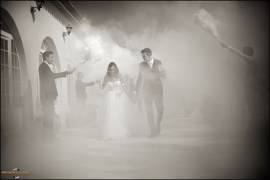O casal recém casado atravessa uma coluna de fumo artificial, no caminho até aos seus convidados na Quinta das Palmeiras em Sintra.