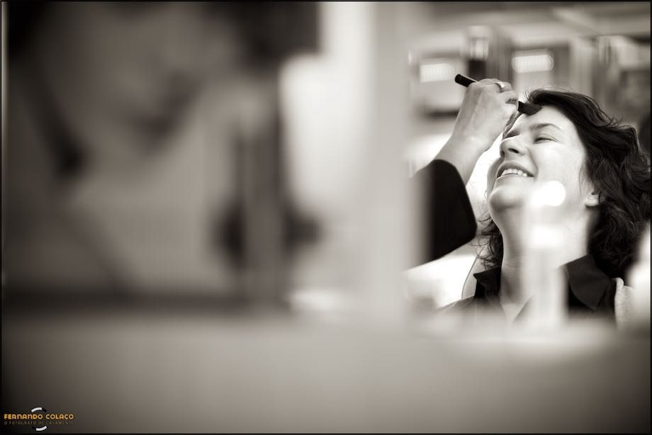 No cabeleireiro, a noiva a ser maquilhada para o casamento, vista por entre os objectos do espaço.