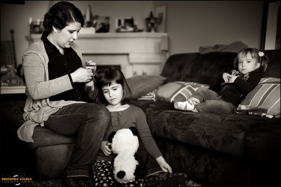 Em casa, e antes de se preparar para o casamento, a noiva penteando a sua filha mais velha, com a mais nova sentada num sofá.