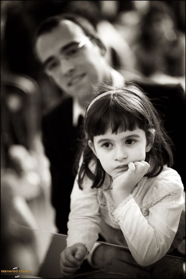 Na mesa da cerimónia do casamento, a filha mais velha do casal sobre a mesa, com a cara apoiada na mão.