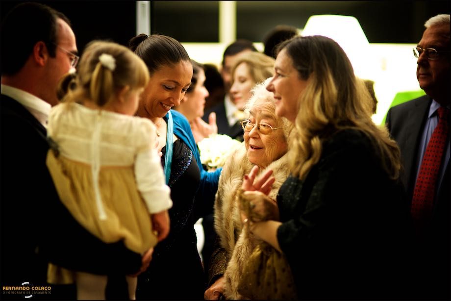 Uma convidada do casamento, com cara de avó, entre outros convidados, conversa com a filha mais nova do casal recém casado.