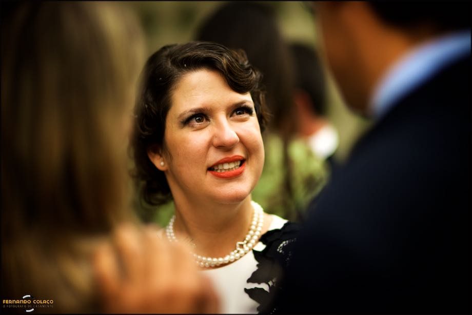 Face da noiva quando conversava com dois convidados, vista entre eles, desfocados no Montes Claros - Lisbon Secret Spot.