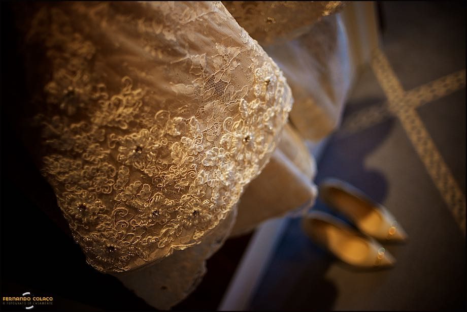 Detalhe das rendas do vestido da noiva com os sapatos em baixo, desfocados.