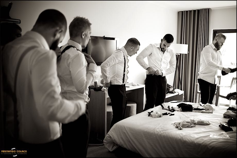 With the baby, son of the bride and groom, lying on the bed flanked by the groom and his friends as they dress for the wedding.
