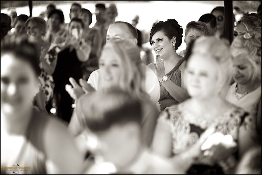 A wedding guest smiles very happily, among the other guests seated during the ceremony at Club Nau in Ferragudo.