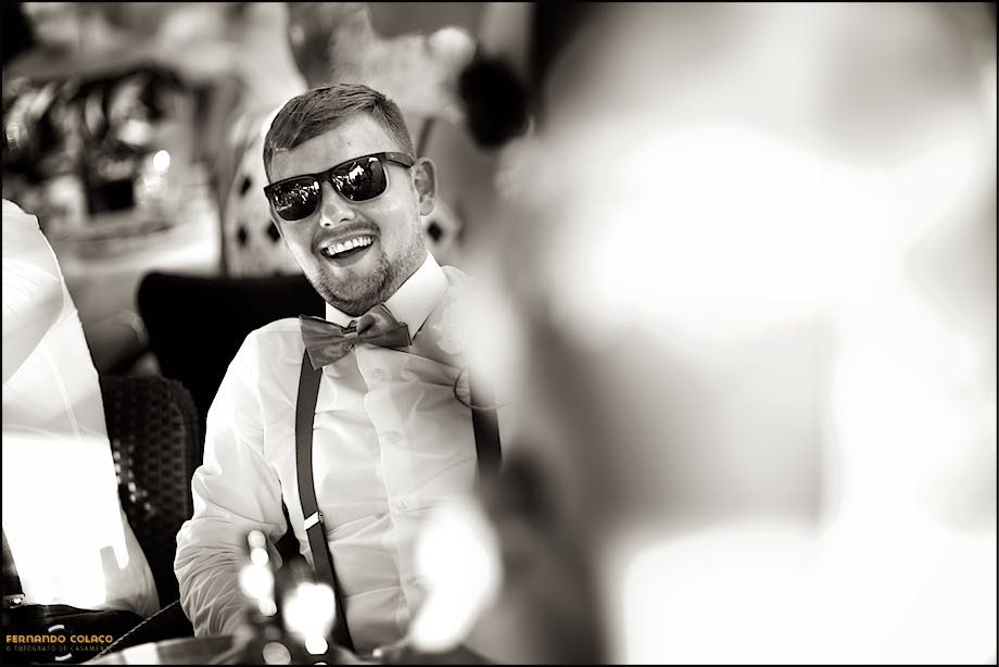 A wedding guest, wearing sunglasses, laughing among others, unfocused.