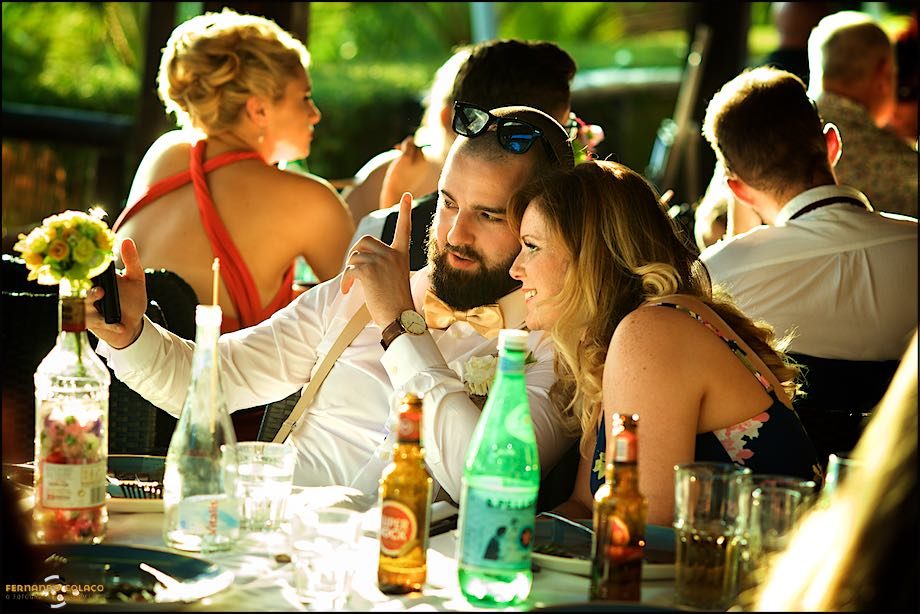 At the wedding meal table, a couple of guests look at a cell phone, smiling.