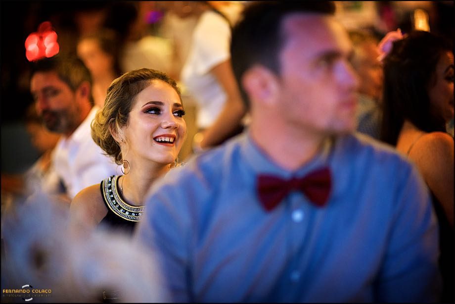 Behind a wedding guest attentive to the speech, unfocused, another guest laughs with satisfaction at what is being said.