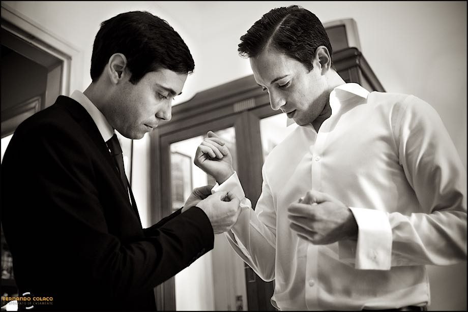 A friend of the groom helps him with the cufflinks of his shirt to get dressed for the wedding.