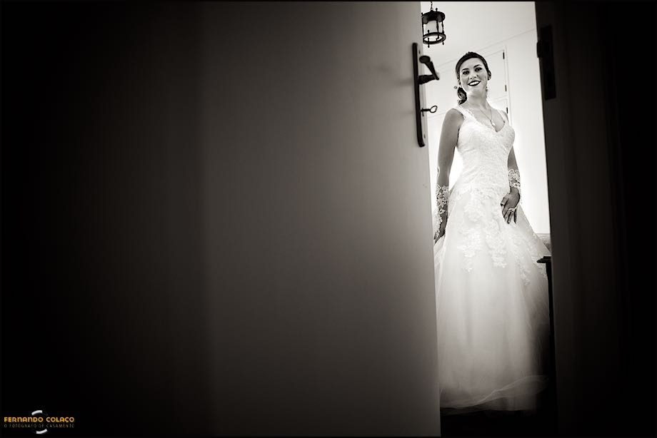 View through the bedroom door, barely closed, the bride, standing, and ready to leave for the wedding ceremony.
