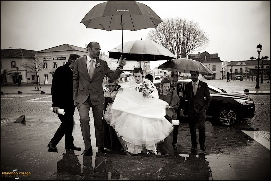 With the floor wet, the bride walks the path to the entrance of the church under umbrellas held by family members.