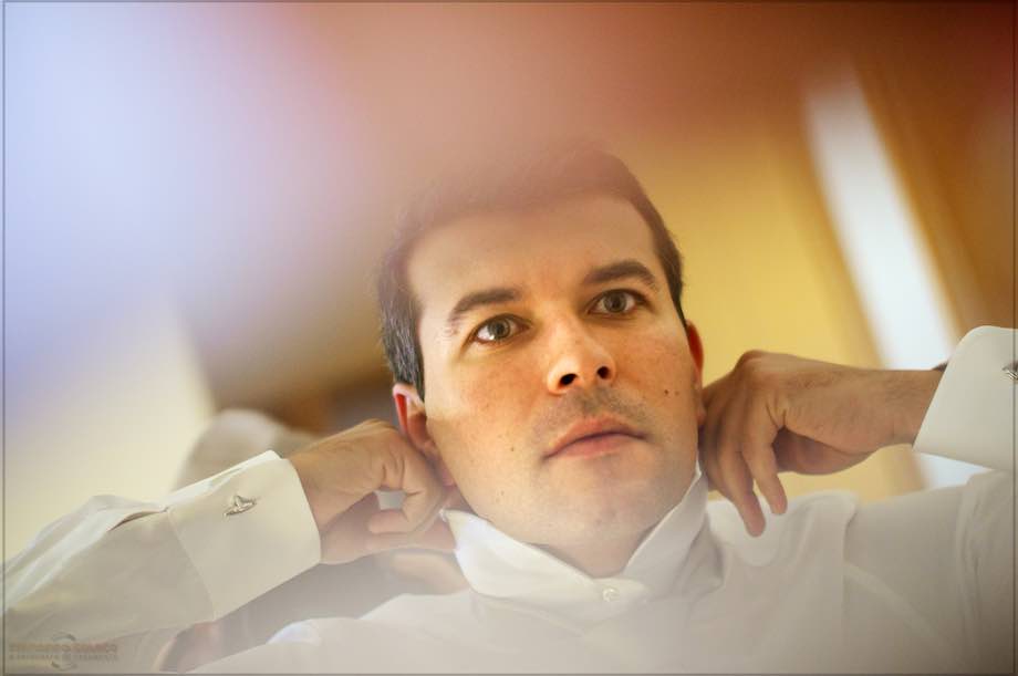 Seeing herself in a mirror, the groom hitting the collar of his shirt as she dresses for the wedding.