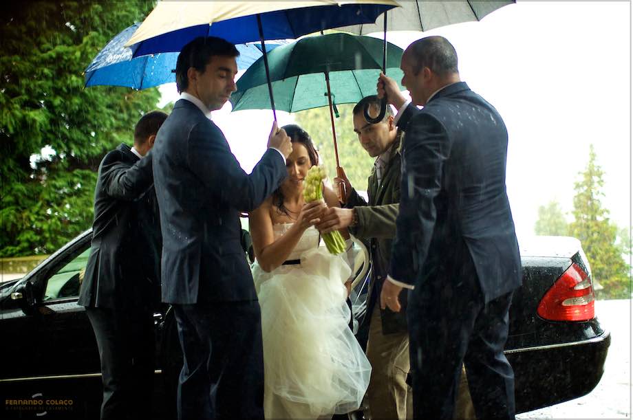 The bride under several umbrellas because of rain as she gets out of the car for the wedding ceremony.