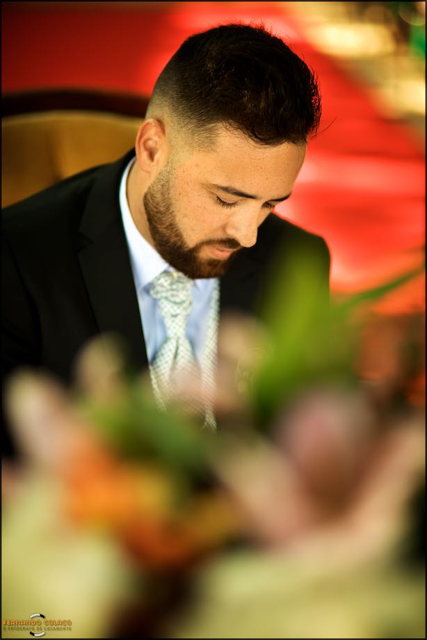 The groom, among red colors, listening at the wedding ceremony.