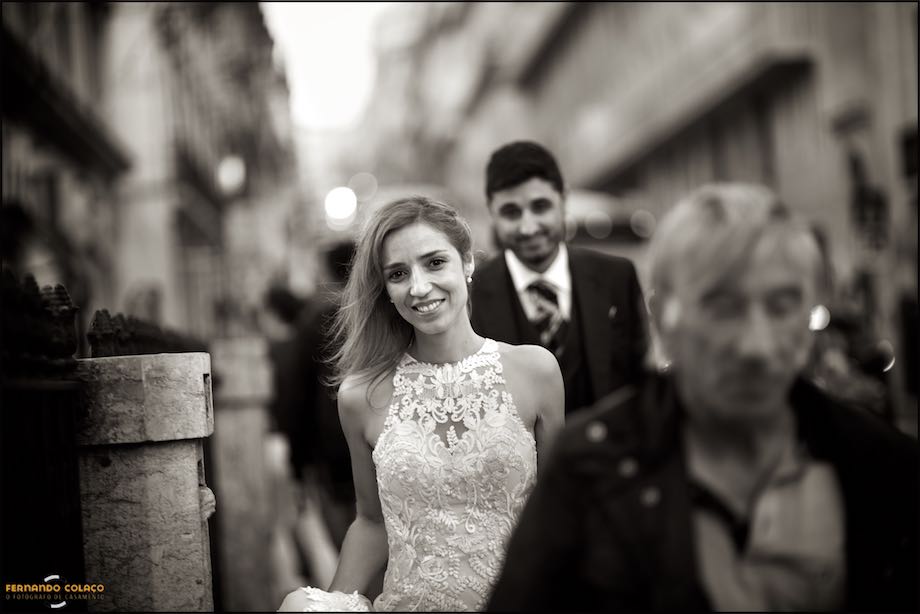 Bride in front of the groom walking down Rua do Alecrim in Lisbon in the midst of other people, out of focus, by the wedding photographer in Portugal.