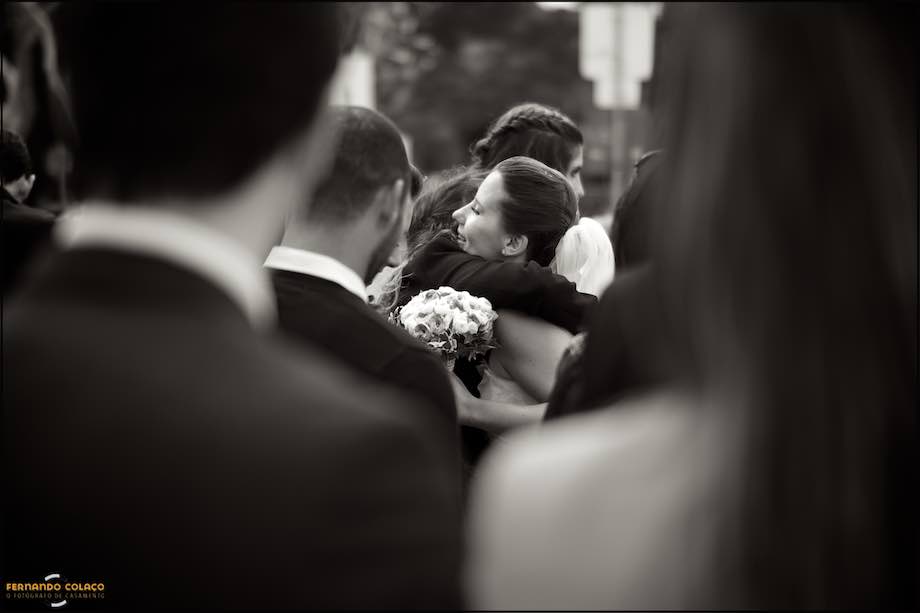 Noiva, no meio de convidados, sendo abraça por uma amiga, pelo fotógrafo de casamento em Cascais.