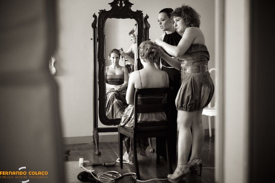 Noiva, sentada enquanto lhe cuidam dos cabelos, e reflectida num espelho à sua frente.