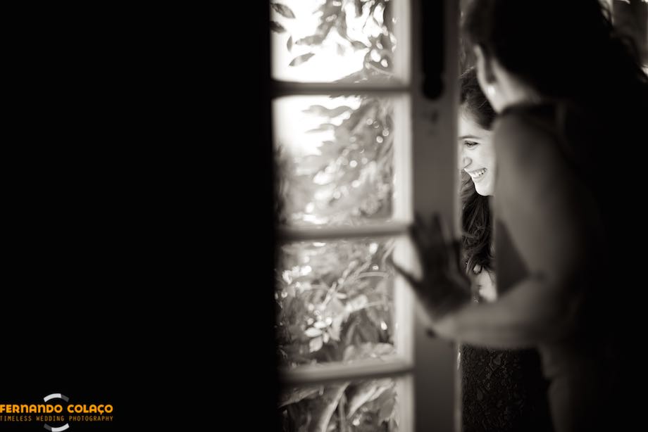 Uma cara sorridente de uma convidada do casamento, vista por entre uma porta envidraçada.