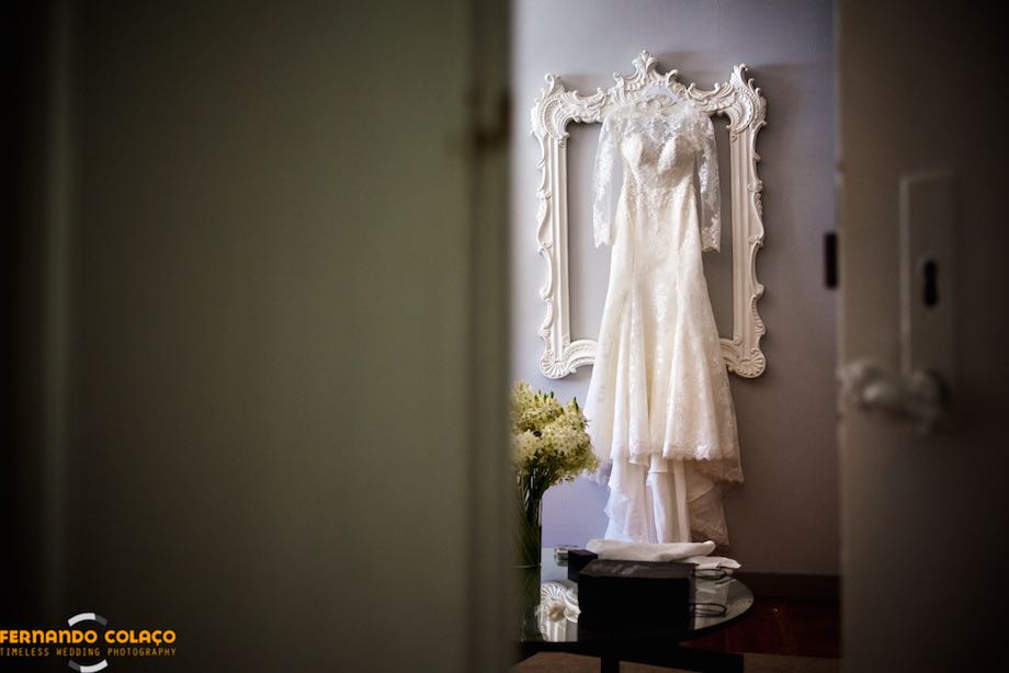 O vestido da noiva pendurado numa moldura de um espelho.